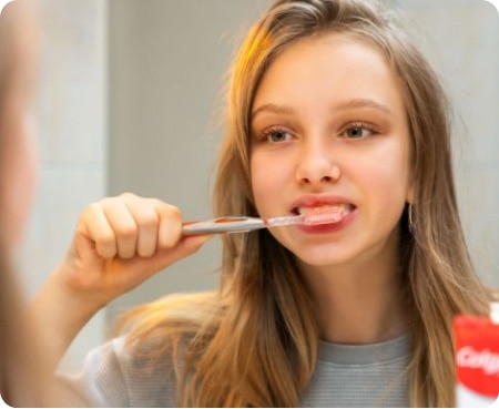 Girl brushing her teeth in front of a mirror as part of a healthy oral health routine.