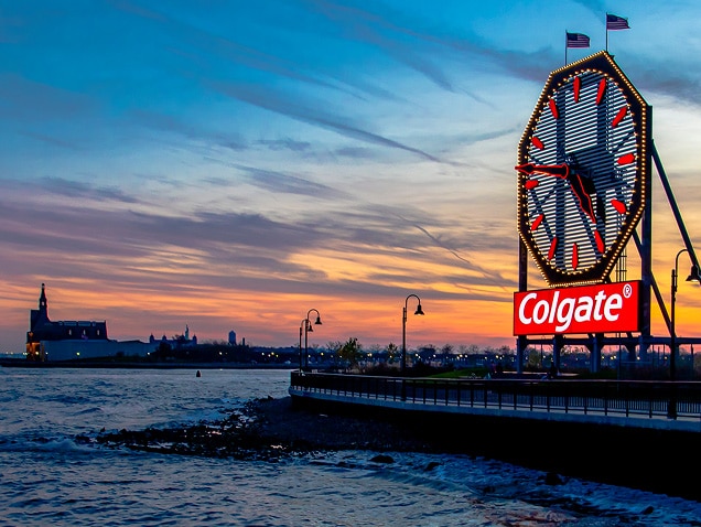 bờ biển, logo Colgate ở phía sau, dưới một chiếc đồng hồ lớn có kim màu đỏ